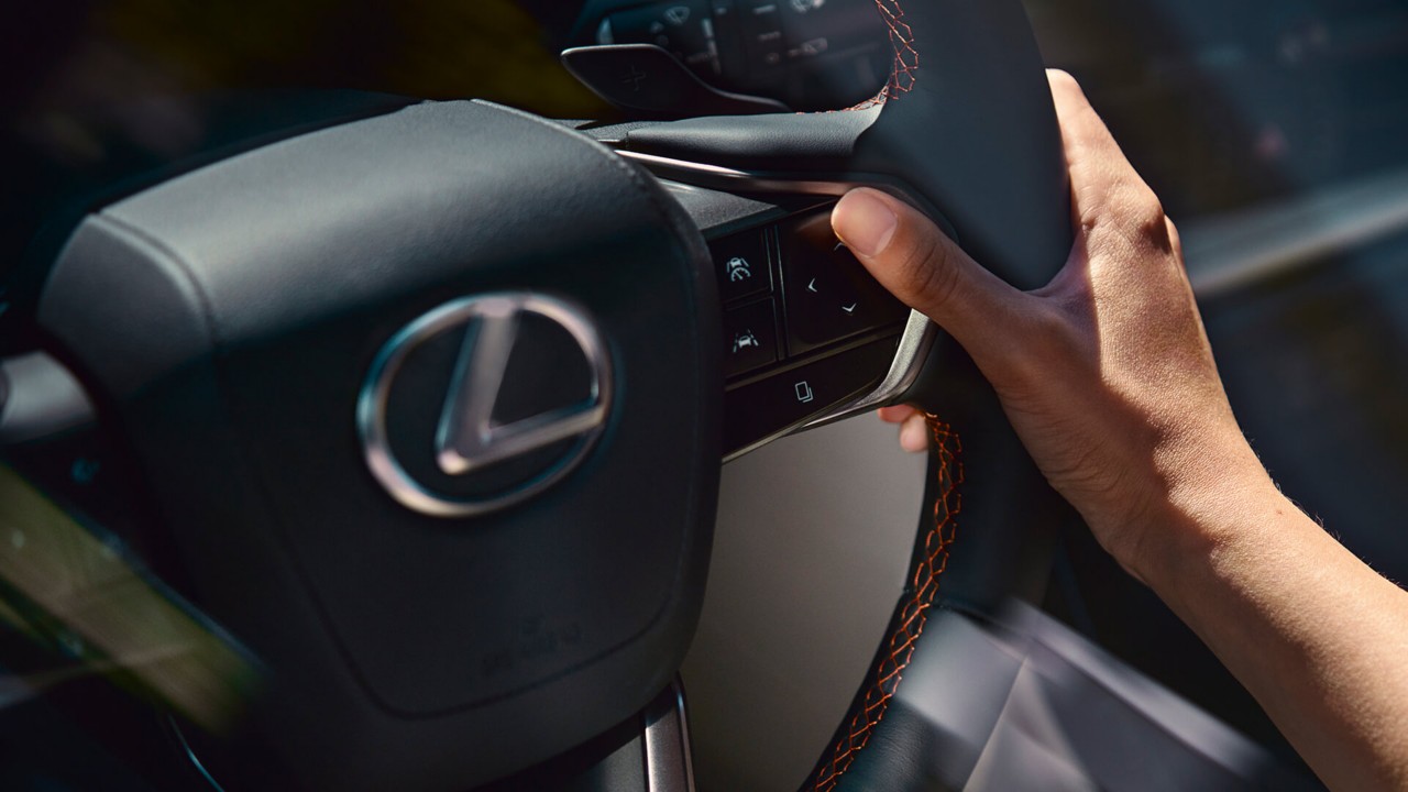A person with their hand on a Lexus steering wheel